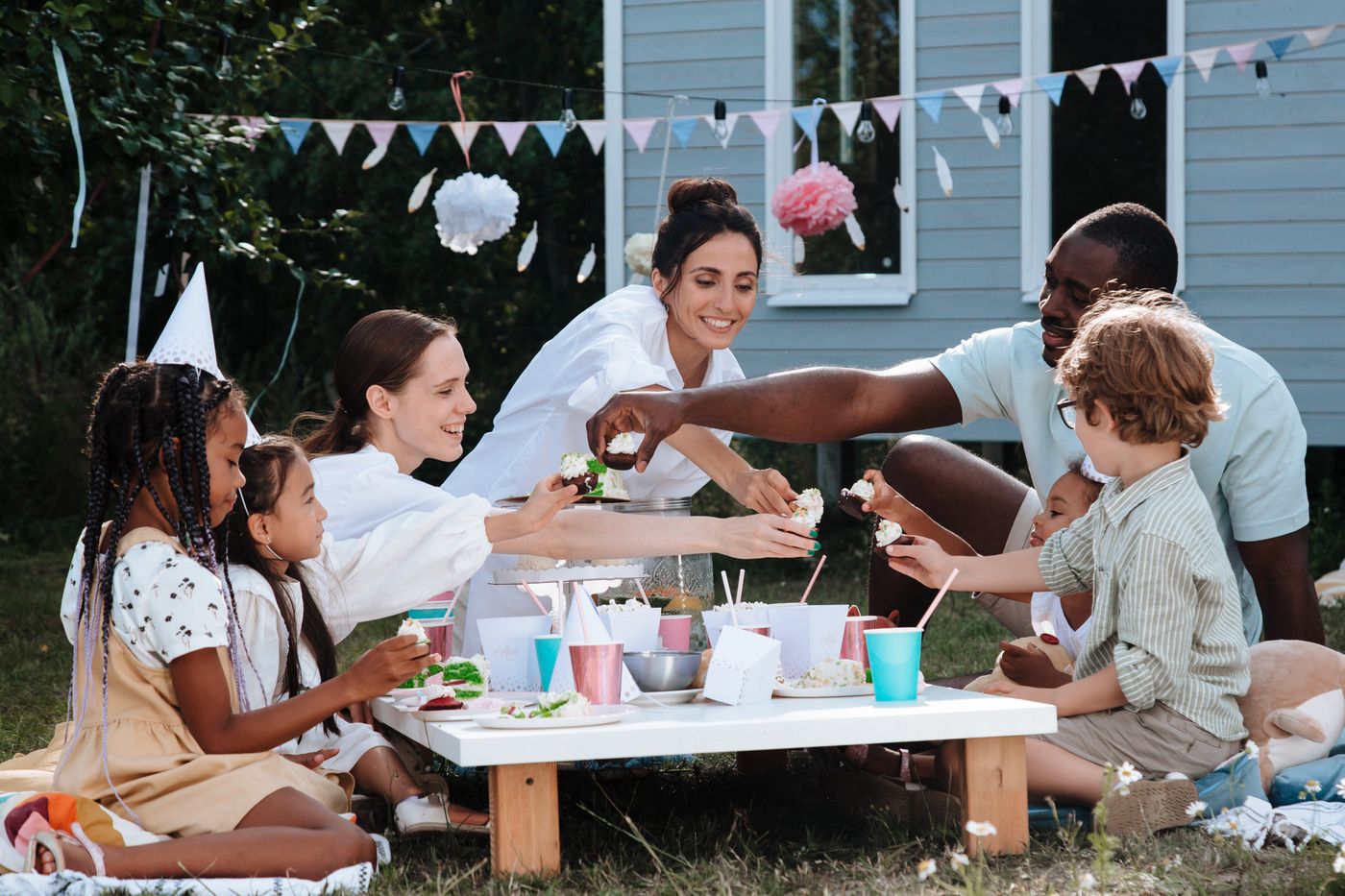 Family and friends sharing birthday cupcakes around a backyard picnic table