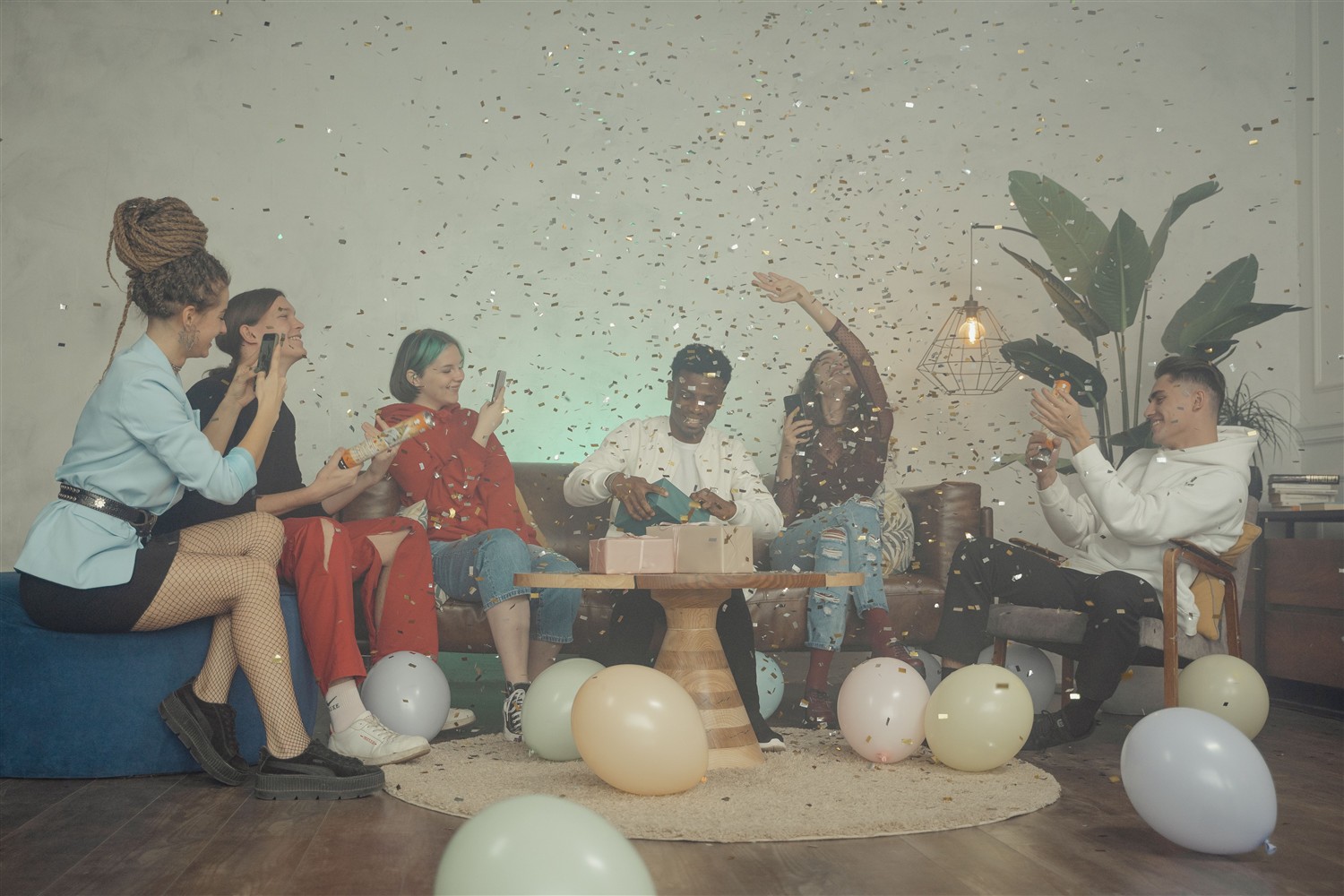 Friends celebrating a birthday with gifts, balloons, and confetti